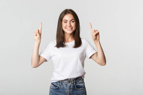 Attractive smiling brunette girl pointing fingers up, showing logo - Foto, Imagem
