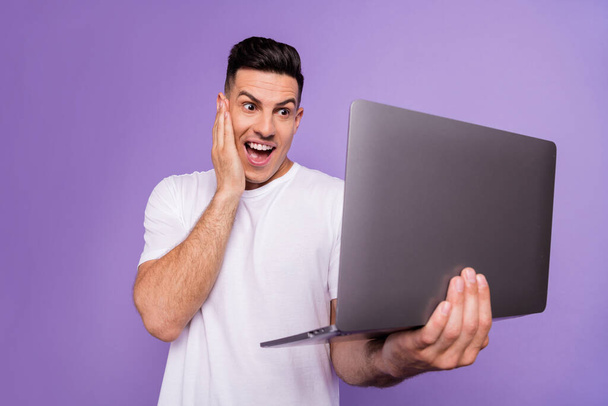 Photo of young excited man happy positive smile surprised look laptop news information isolated over purple color background - Фото, зображення