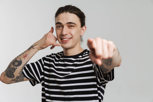 Young white man with earring gesturing and pointing finger at camera isolated over white background - Valokuva, kuva