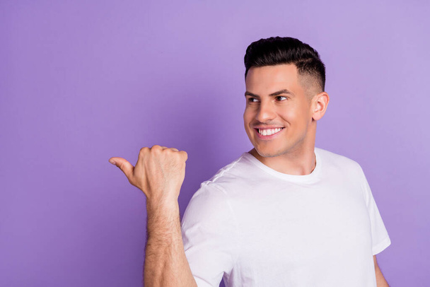 Photo of young charming positive happy man point finger empty space smile isolated on purple color background - Foto, immagini