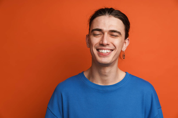 Young white man with earring posing and laughing at camera isolated over orange background - Φωτογραφία, εικόνα