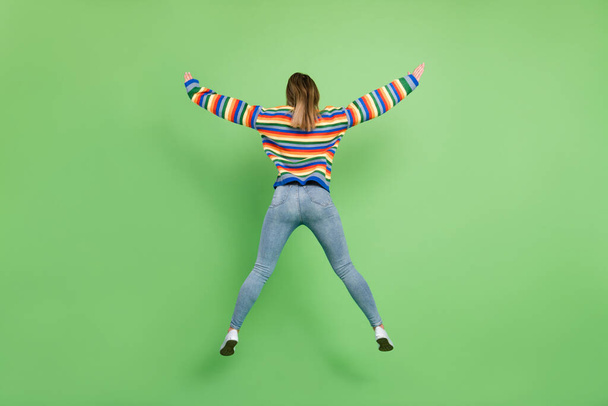 Comprimento total do corpo tamanho raro vista foto menina saltando vestindo roupas casuais isolado pastel cor verde fundo - Foto, Imagem