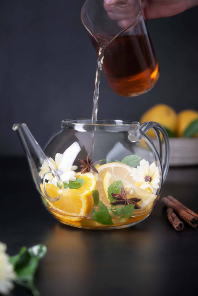 Fruit citrus tea and glass teapot on black background. Herbal calendula healthy tea drink - Фото, изображение