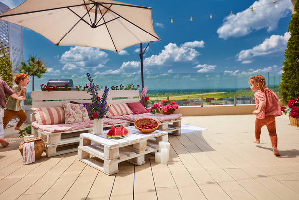 wooden pallet furniture on rooftop patio with running kids at sunny summer day - Foto, Imagen