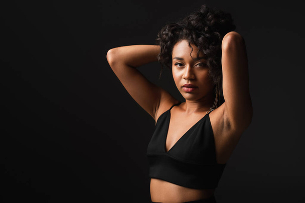 fashionable african american woman in satin and sexy crop top posing isolated on black  - Zdjęcie, obraz