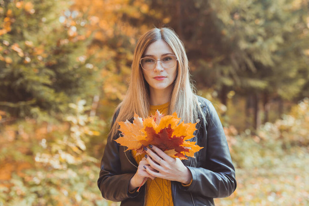 秋の公園で紅葉を持つかわいい笑顔の女性。季節、ライフスタイル、レジャーのコンセプト. - 写真・画像