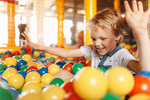 Μαθητές διασκεδάζουν στην παιδική χαρά του πάρκου. Το χαρούμενο αγόρι παίζει στην παιδική χαρά. Αγόρια και κορίτσια που παίζουν με πολύχρωμες πλαστικές μπάλες σε μεγάλη στεγνή πισίνα κωπηλασίας στο κέντρο παιχνιδιού - Φωτογραφία, εικόνα