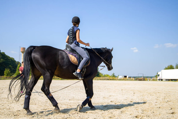 Das Mädchen reitet auf einem schwarzen Pferd. Reitstunde. - Foto, Bild