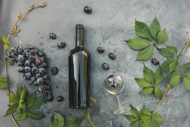 Bir şişe kırmızı şarap, yeşil üzüm, şarap kadehi ve olgun üzümlü eskimiş taş masa arkaplanı. Metin için üst görünüm kopyalama alanı. Şarap dükkanı şarap dükkanı ya da şarap tatma konsepti - Fotoğraf, Görsel