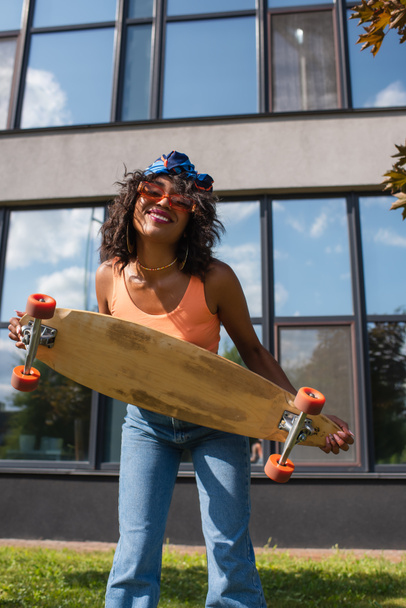 positive african american woman holding longboard near building outside  - Photo, Image