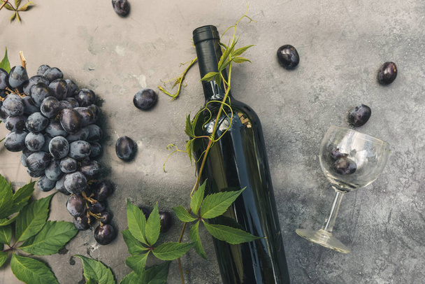 Butelka czerwonego wina, zielona winorośl, kieliszek do wina i dojrzałe winogrona na tle ciemnego kamiennego stołu vintage. Widok z góry kopiuj miejsce na tekst. Koncepcja winiarni winiarni lub degustacji wina - Zdjęcie, obraz