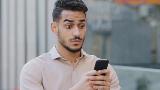Hispanic amazed businessman receiving sms message offer opportunity, arabian happy man reading good news in smartphone. Excited overjoyed male winner outdoors celebrating success mobile phone victory - Footage, Video
