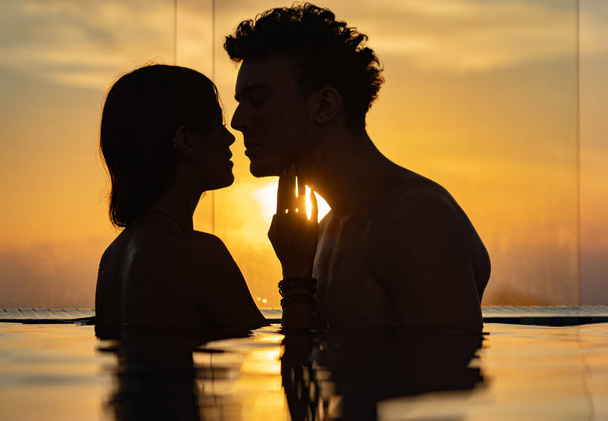 Silhouette of Loving couple in the infinity pole water during sunset. Romance and relationship - Zdjęcie, obraz