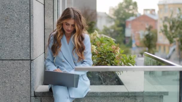 Kaukázusi üzletasszony fiatal lány gépel laptop billentyűzeten ül a tetőteraszon a városban. Női vállalkozó professzionális felhasználó dolgozó számítógép notebook ülni szabadban dolgozik online pc app - Felvétel, videó