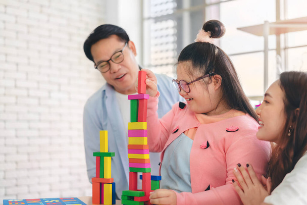 Happy asian father and mother playing education toy with their daughter down syndrome child in living room, Activity happy family lifestyle concept. - 写真・画像