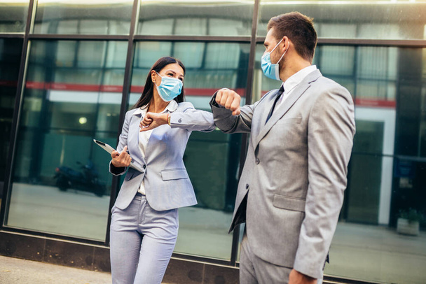 Business man and woman with safety masks greeting with elbow bump in front of office building.  - Photo, image