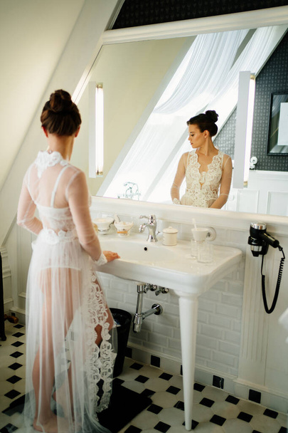 a beautiful young woman in a silk robe by the mirror in the bathroom.  - Фото, изображение