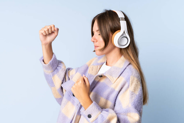 Νεαρή Λιθουανή γυναίκα απομονωμένη σε μπλε φόντο ακούγοντας μουσική και χορεύοντας - Φωτογραφία, εικόνα