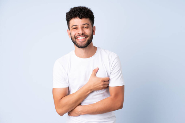 Young Moroccan man isolated on blue background smiling a lot - Foto, afbeelding