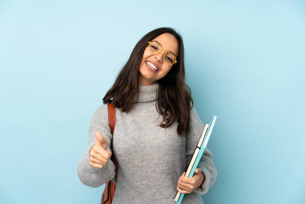 Young mixed race woman going to school isolated on blue background with thumbs up because something good has happened - Photo, Image