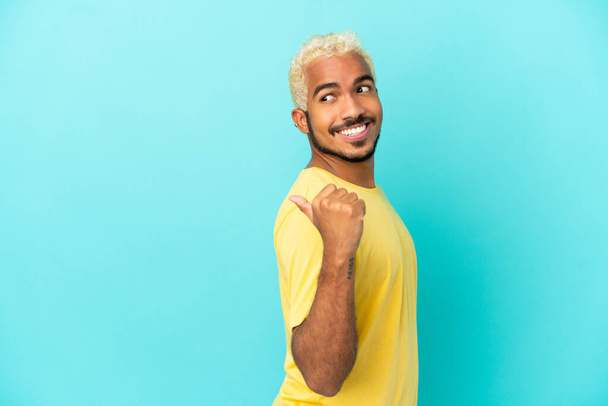 Young Colombian handsome man isolated on blue background pointing to the side to present a product - Fotó, kép
