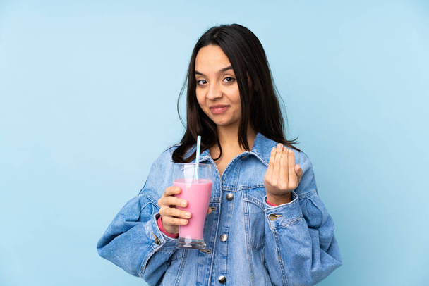 Jonge vrouw met aardbeien milkshake over geïsoleerde blauwe achtergrond uitnodigen om te komen met de hand. Blij dat je gekomen bent. - Foto, afbeelding