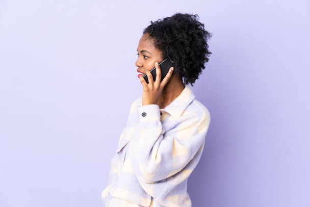 Fiatal afro-amerikai nő elszigetelt lila háttér tartja a beszélgetést a mobiltelefon valakivel - Fotó, kép