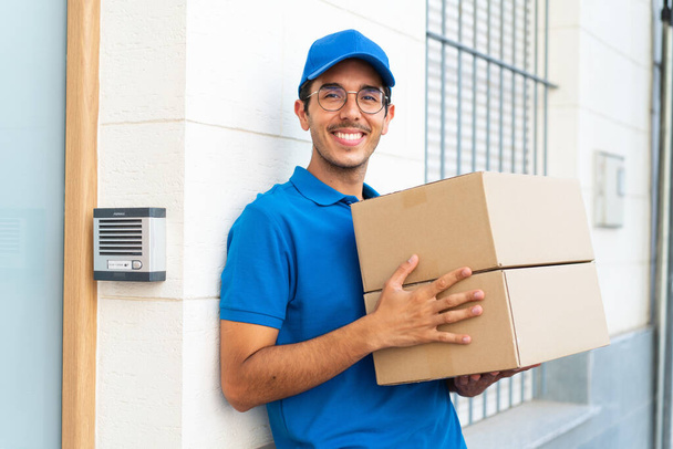 Молодой доставщик на открытом воздухе держит коробки с радостным выражением лица - Фото, изображение