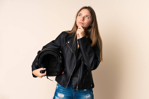 Young Lithuanian woman holding a motorcycle helmet isolated on beige background and looking up - Foto, imagen