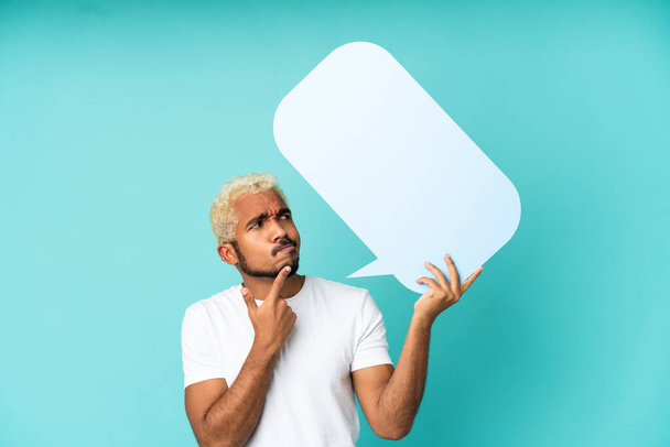 Young Colombian handsome man isolated on blue background holding an empty speech bubble and thinking - Zdjęcie, obraz