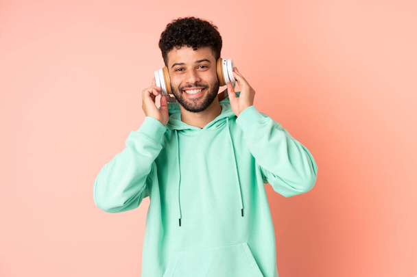 Young Moroccan man isolated on pink background listening music - Zdjęcie, obraz