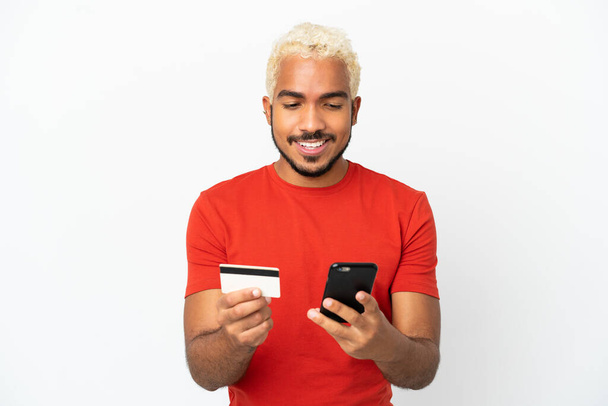 młody Kolumbijczyk przystojny mężczyzna odizolowany na białym tle zakup z telefonu komórkowego z karty kredytowej - Zdjęcie, obraz