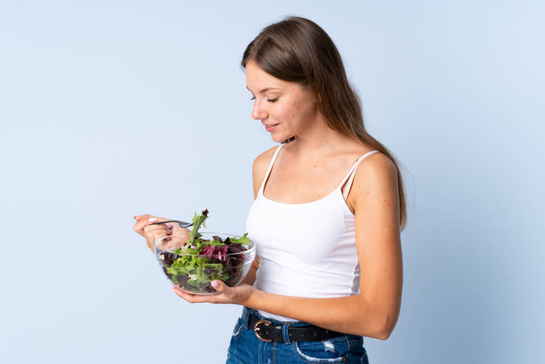 Junge Litauerin isoliert auf blauem Hintergrund mit einer Schüssel Salat mit glücklichem Gesichtsausdruck - Foto, Bild