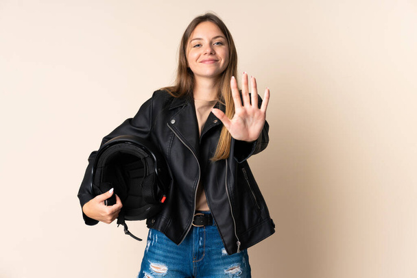 Young Lithuanian woman holding a motorcycle helmet isolated on beige background counting five with fingers - Photo, Image