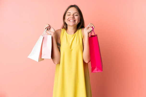 Young Lithuanian woman isolated on pink background holding shopping bags and smiling - Фото, изображение