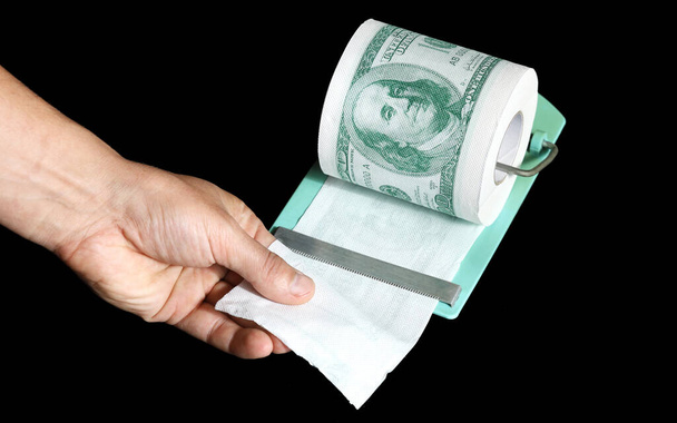 Mano rasgar parte de rollo de papel higiénico en forma de dólares, concepto de déficit y alto costo de los bienes, sobre fondo negro - Foto, Imagen