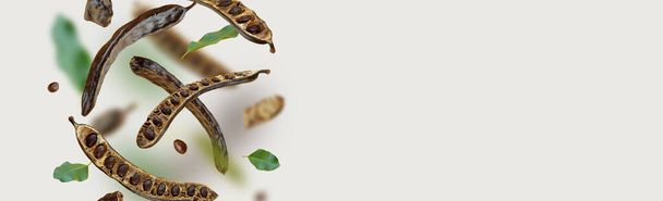 Creative composition. Floating Organic carob pods, seeds, leafs. food background. Natural vegan eating. Flying Organic product. Levitation concept, falling healthy sweets. horizontal banner.Copy space - Photo, Image