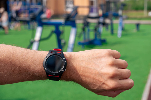 look at a smartwatch on a man's hand against the background of outdoor gym machines - Photo, Image