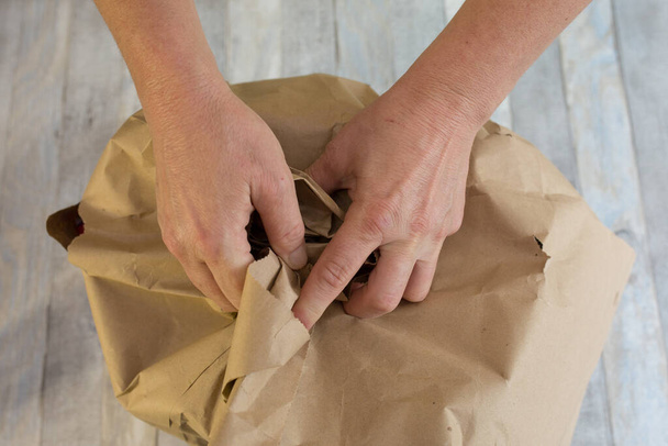 Las manos femeninas están envolviendo bolsas de papel de los alimentos entregados. Papel de desecho se coloca en contenedores de papel separados para el reciclaje. - Foto, Imagen