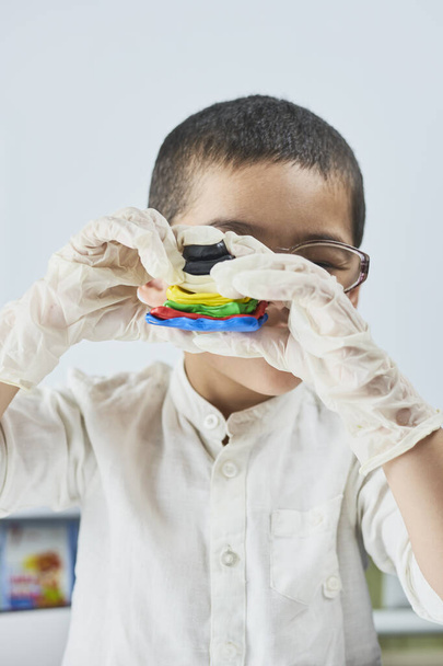 Дитина в окулярах і рукавичках грає з пластиліном
 - Фото, зображення