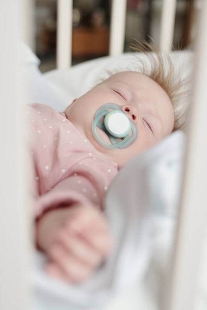 Peaceful infant with pacifier in mouth having rest in the middle of the day - Фото, изображение