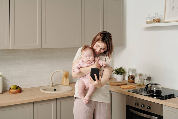 Jeune mère avec smartphone tenant sa fille bébé - Photo, image