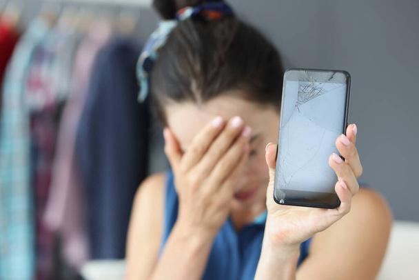 Smutná žena zakrývá oči rukou a drží rozbitý mobilní telefon detailní - Fotografie, Obrázek