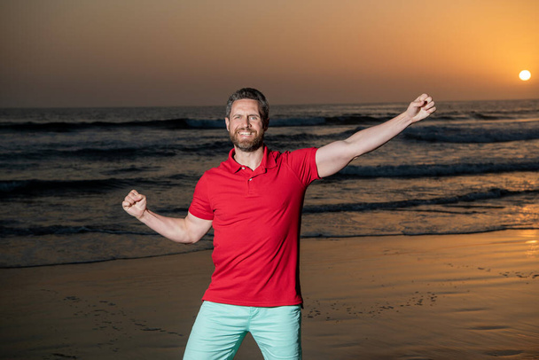 ευτυχισμένος άνθρωπος γιορτάζει την επιτυχία πάνω από τη θάλασσα στην ηλιόλουστη καλοκαιρινή παραλία, ευτυχία - Φωτογραφία, εικόνα