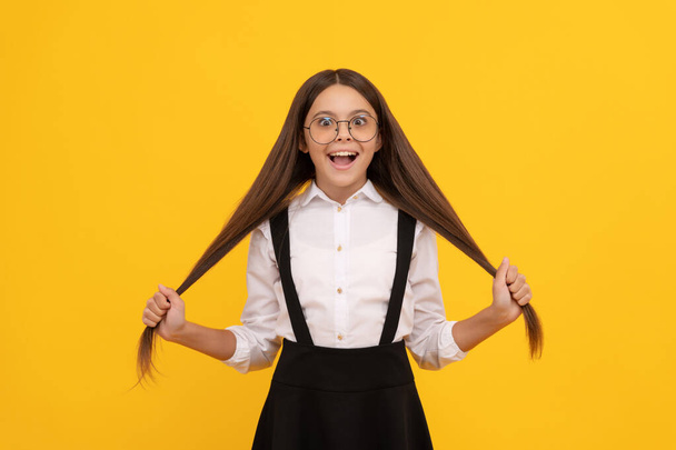 onnellinen lapsi pitää pitkät hiukset koulussa yhtenäinen ja lasit visio suojelua, hiustenhoito - Valokuva, kuva