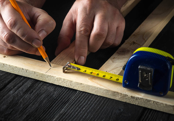 Un carpintero hace marcas de lápiz en un bloque de madera. Las manos del maestro de cerca en el trabajo. Ambiente de trabajo en un taller de carpintería - Foto, Imagen