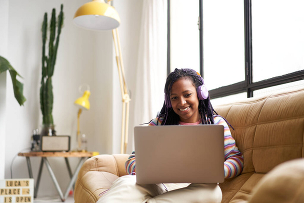Jonge Afro-Amerikaanse vrouw die van thuis uit pendelt. Gebruik van een laptop, chatten of surfen op internet. - Foto, afbeelding