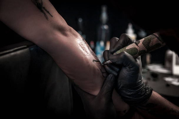 Een horizontaal schot van een tatoeëerder die een tatoeage doet bij een vrouw op haar arm, de tatoeëerder is zeer geconcentreerd terwijl hij de tattoo machine bedient. - Foto, afbeelding