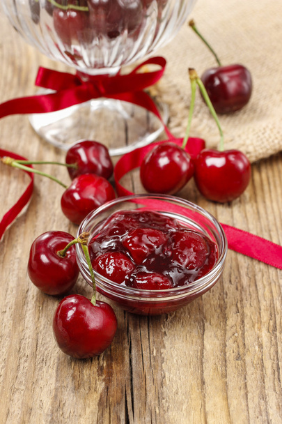Bowl of cherry jam on wooden table and fresh cherries around - Фото, зображення