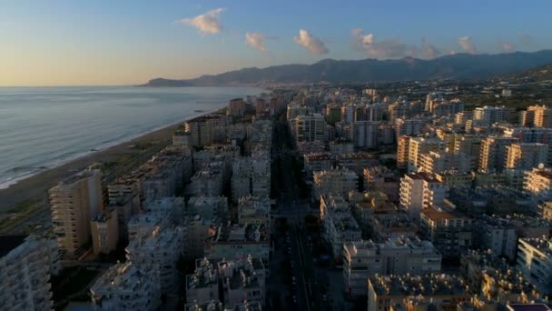 Mahmultar o zachodzie słońca. Prowincja Antalya w Turcji. Latający helikopter nad miastem i wybrzeżem z rozbijającymi się falami Morza Śródziemnego i otoczony górami Taurus. - Materiał filmowy, wideo